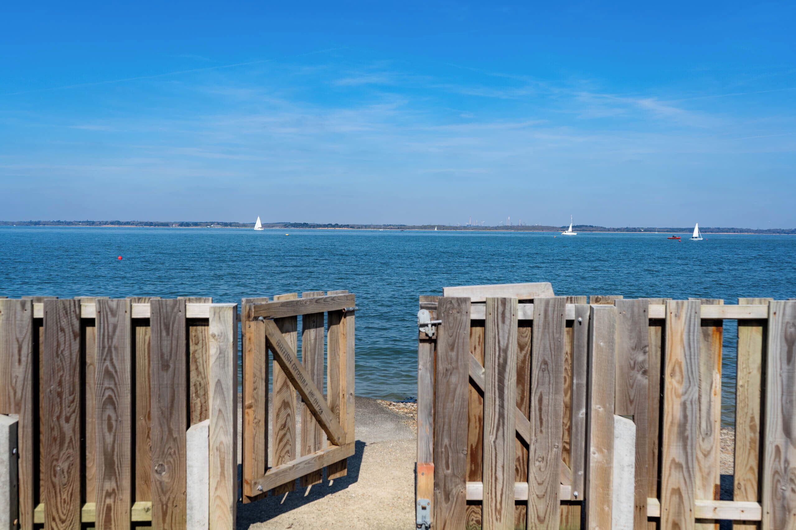 A wooden dock leading into a calm body of water with sailboats in the distance.