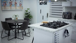 A modern kitchen with a central island, a dining table with chairs, and a painting on the wall. - Salt Water Private Pool House W/ Ocean View, WiFi, Air Cond, Generator, Solar E. (Naguabo)