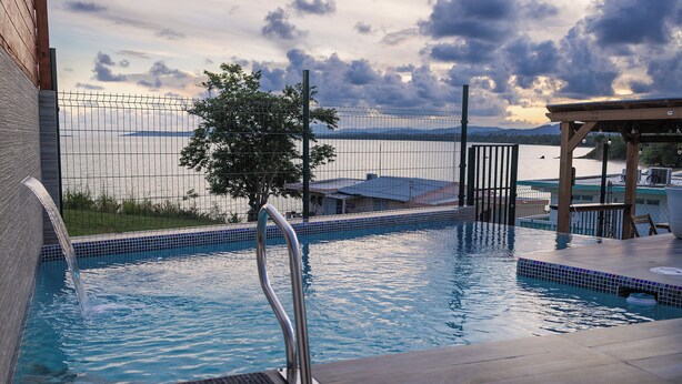 A swimming pool with a metal ladder, surrounded by a fence, and overlooking a body of water with distant mountains. - Salt Water Private Pool House W/ Ocean View, WiFi, Air Cond, Generator, Solar E. (Naguabo)