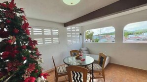 A dining area with a round glass table and four wooden chairs, a decorated Christmas tree, and large windows with a view of a parking lot and buildings. - Quiet & comfortable, 3/2, 5 beds free parking, sleep 9 (Ceiba)
