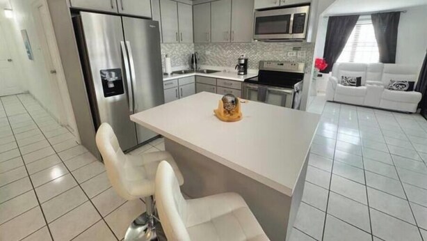 A modern kitchen with stainless steel appliances, a central island with bar stools, and a white tiled floor. - Quiet & comfortable, 3/2, 5 beds free parking, sleep 9 (Ceiba)