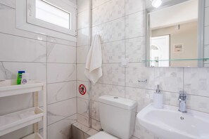 A bathroom with a toilet, sink, and shelves; a no-entry sign; and a window. - Serenity and Views - Beachside Escape (Agia Kiriaki)