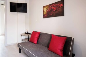 A modern living room with a grey sofa, red cushions, a flat-screen TV, and a painting on the wall. - Serenity and Views - Beachside Escape (Agia Kiriaki)