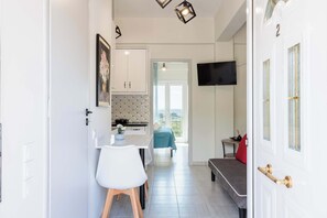 A modern kitchen with white cabinets, a dining area with a white table and chairs, a sofa, and a TV mounted on the wall.