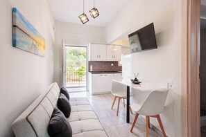 Une cuisine moderne avec des meubles blancs, un coin repas avec des chaises blanches et un canapé agrémenté de coussins.