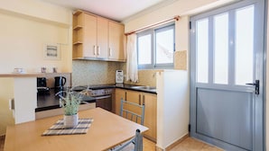 A compact kitchen with wooden cabinets, a tiled backsplash, a dining table with chairs, and a window with curtains. - Studio with Balcony Steps from Filiatra Square (Filiatra)