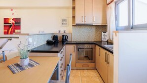 A compact kitchen with a stove, oven, and a small dining area with a table and a potted plant. - Studio with Balcony Steps from Filiatra Square (Filiatra)
