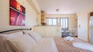 A hotel room with a bed, a painting on the wall, a kitchen area, and a dining table. - Studio with Balcony Steps from Filiatra Square (Filiatra)