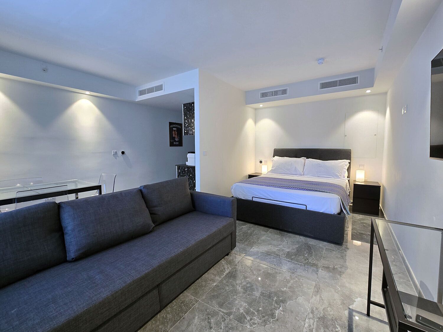 Une chambre à coucher moderne avec un lit, un canapé gris et une table en verre.