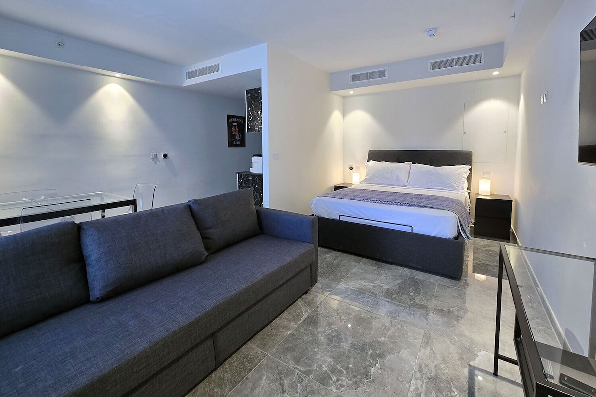 A modern bedroom with a bed, a grey sofa, and a glass table.