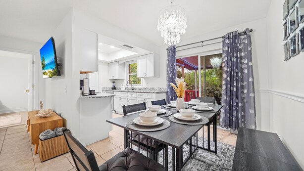 Une cuisine moderne avec des meubles blancs, un coin repas doté d’une table en bois foncé, dressée pour quatre personnes, et un lustre.