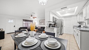 Une cuisine moderne équipée d’un four encastré, d’un réfrigérateur et d’un four à micro-ondes. On y trouve un coin repas avec une table dressée pour quatre personnes, ainsi qu’un salon avec un canapé et une table basse.