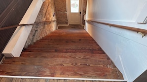 Un escalier en bois avec une rampe, une porte en bas et un mur de briques sur un côté.