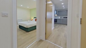 A hotel room with a bed, a bedside table, and a nightstand. There is a kitchen area visible through an open door. - Beauchamp House, 2-bed apartment Covstays (Coventry)