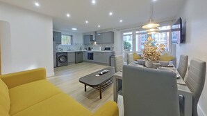 A modern living room with a sofa, a dining table with chairs, and a kitchen in the background. - Beauchamp House, 2-bed apartment Covstays (Coventry)
