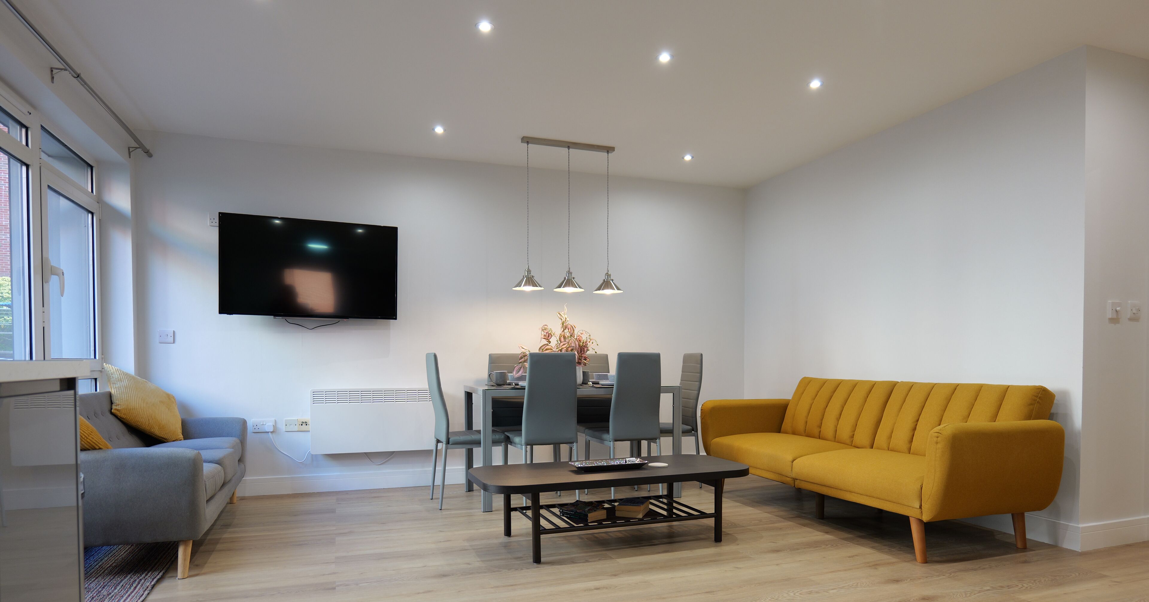 Una sala moderna con sofá, mesa de comedor, sillas y televisor montado en la pared.
