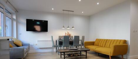 Una sala moderna con sofá, mesa de comedor, sillas y televisor montado en la pared.