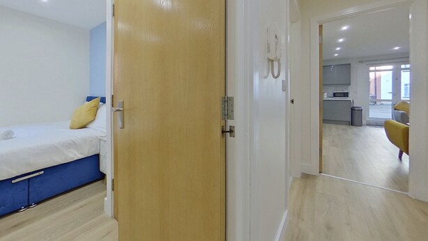 A modern hotel room with a bed, a wooden door, and a view into the kitchen area. - Beauchamp House, 2-bed apartment Covstays (Coventry)