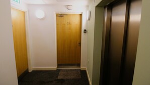 Un pasillo con una puerta de madera marcada con el número 29, un ascensor y piso cubierto de alfombra.