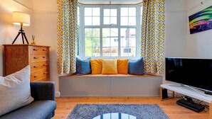A cozy living room with a sofa, a TV, and a window seat with cushions. - Stylish and Modern Flat with Free Parking | Pass the Keys (Cambridge)