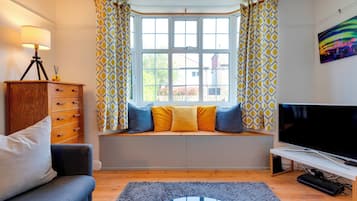 A cozy living room with a sofa, a TV, and a window seat with cushions.