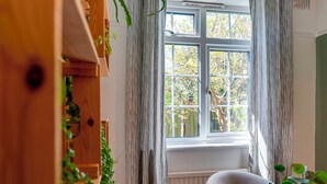 A room with a large window, a wooden cabinet with plants, and a round table. - Stylish and Modern Flat with Free Parking | Pass the Keys (Cambridge)