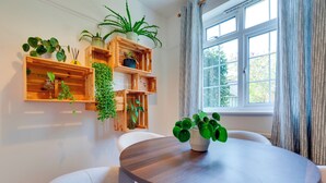 A dining area with a round table, white chairs, and wooden shelves with plants. - Stylish and Modern Flat with Free Parking | Pass the Keys (Cambridge)