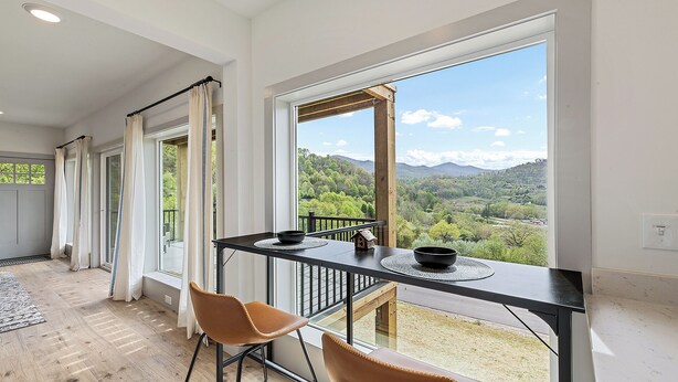 A dining area with a table, chairs, and a view of a forested landscape.