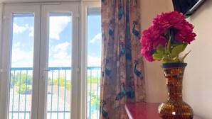 A room with a balcony door, a vase with flowers, and a patterned curtain.