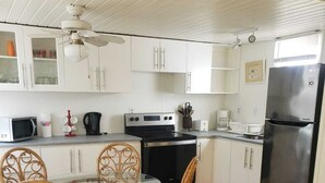 Een keuken met witte kastjes, een roestvrijstalen koelkast, een magnetron, een fornuis en een eettafel met rieten stoelen.
