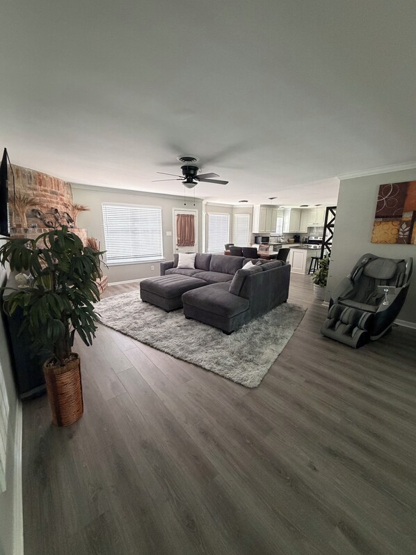 A spacious living room with a grey sectional sofa, a large potted plant, and a massage chair.