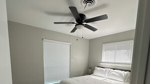 A bedroom with a bed, ceiling fan, and two windows with blinds. - Pinewoods Hideaway – Quiet Comfort Near It All (Spring)