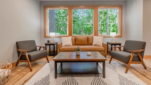 Una sala de estar moderna con un sofá, dos sillones, una mesa de centro y un ventanal con vistas a zonas verdes.