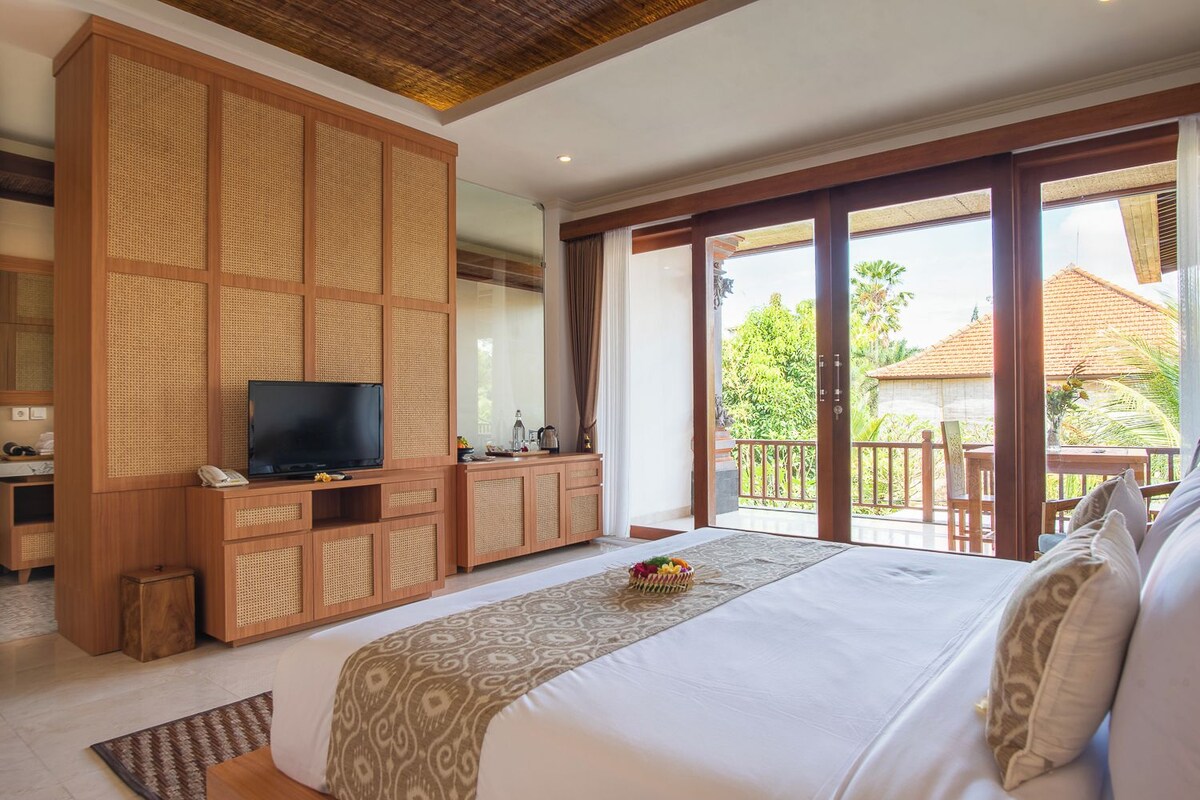 Ein Schlafzimmer mit einem großen Bett, einem Fernseher, einem Holzschrank und einem Balkon mit Blick ins Grüne.
