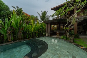 Ein Pool mit geschwungener Kante, umgeben von üppiger Vegetation und einem Gebäude mit Balkon.