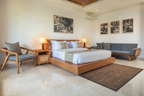 A modern hotel room with a wooden bed, two bedside tables with lamps, a grey sofa, and three framed pictures on the wall. - Budhi Ayu Suite (Ubud)