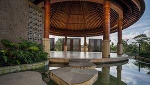 A circular pavilion with a wooden roof, surrounded by a reflective pool and lush greenery. - Budhi Ayu Suite (Ubud)