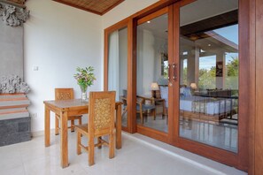 Une pièce comprenant une table et des chaises en bois, un vase rempli de fleurs et une porte-fenêtre coulissante donnant sur un balcon avec vue sur l’extérieur.