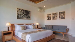 A modern bedroom with a large bed, two bedside tables with lamps, a grey sofa, and three framed pictures on the wall. - Budhi Ayu Suite (Ubud)