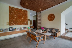 A modern living room with a sofa, chairs, a coffee table, decorative wall panels, and a wooden ceiling. - Budhi Ayu Suite (Ubud)