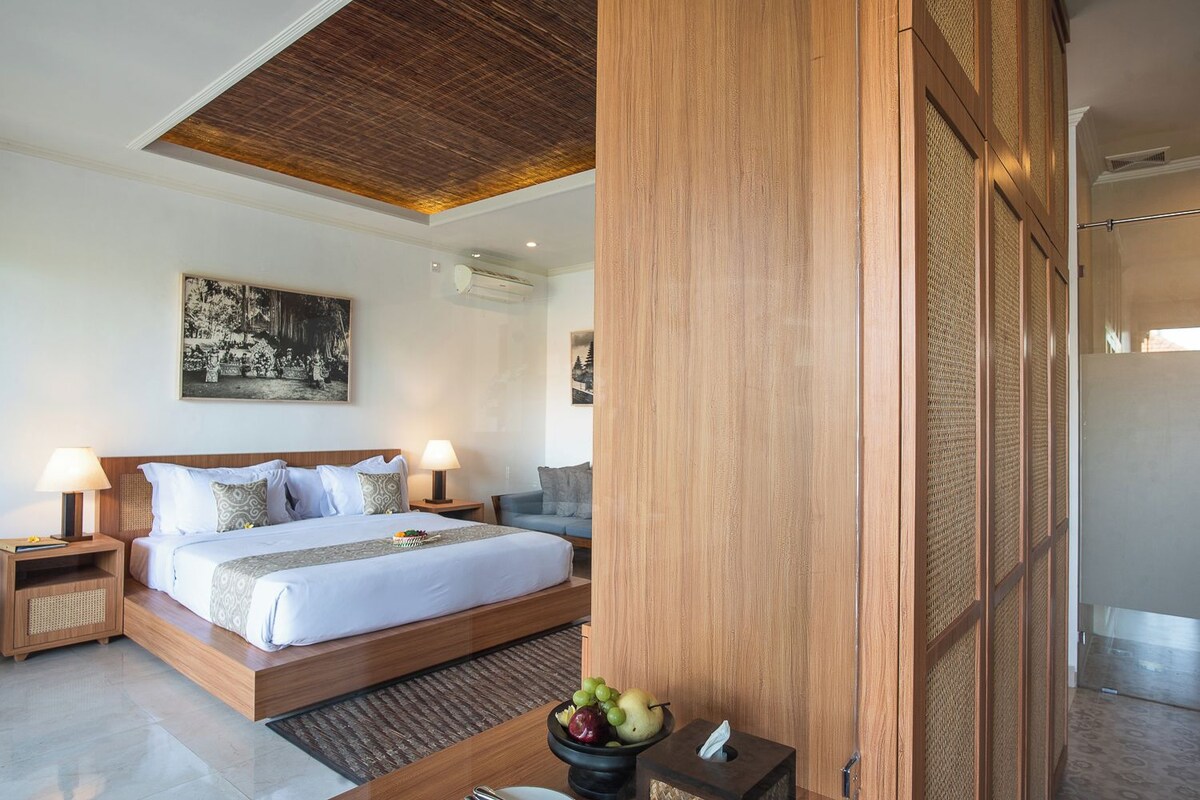 A modern bedroom with a large bed, wooden headboard, bedside tables with lamps, and a wall-mounted air conditioner.