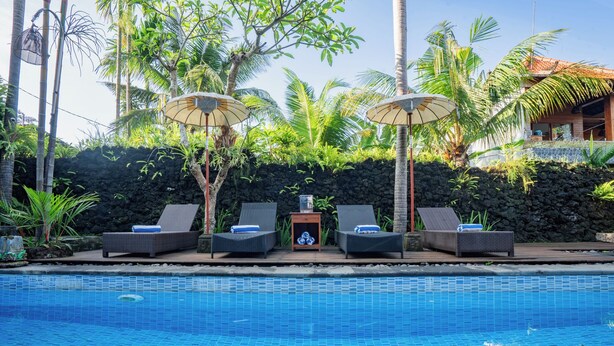A poolside area with lounge chairs and umbrellas, surrounded by tropical plants and a stone wall. - Budhi Ayu Suite (Ubud)