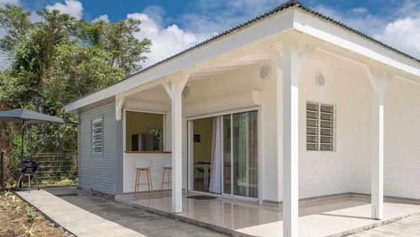 A white single-story house with a covered patio, a sliding glass door, and a small outdoor seating area.