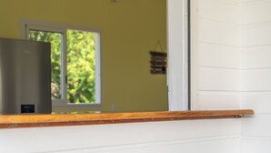 A room with a white wall, a window with a view of greenery, and a wooden ledge.