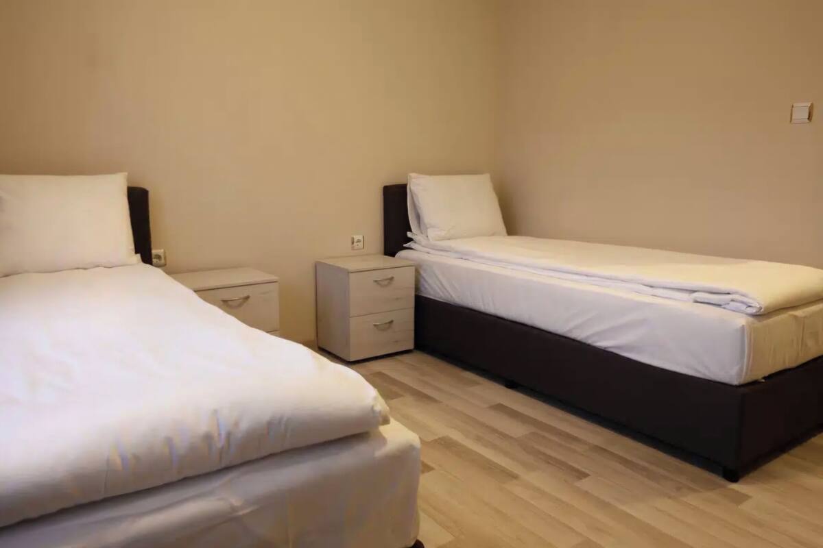A bedroom with two single beds, a bedside table, and a small drawer unit.