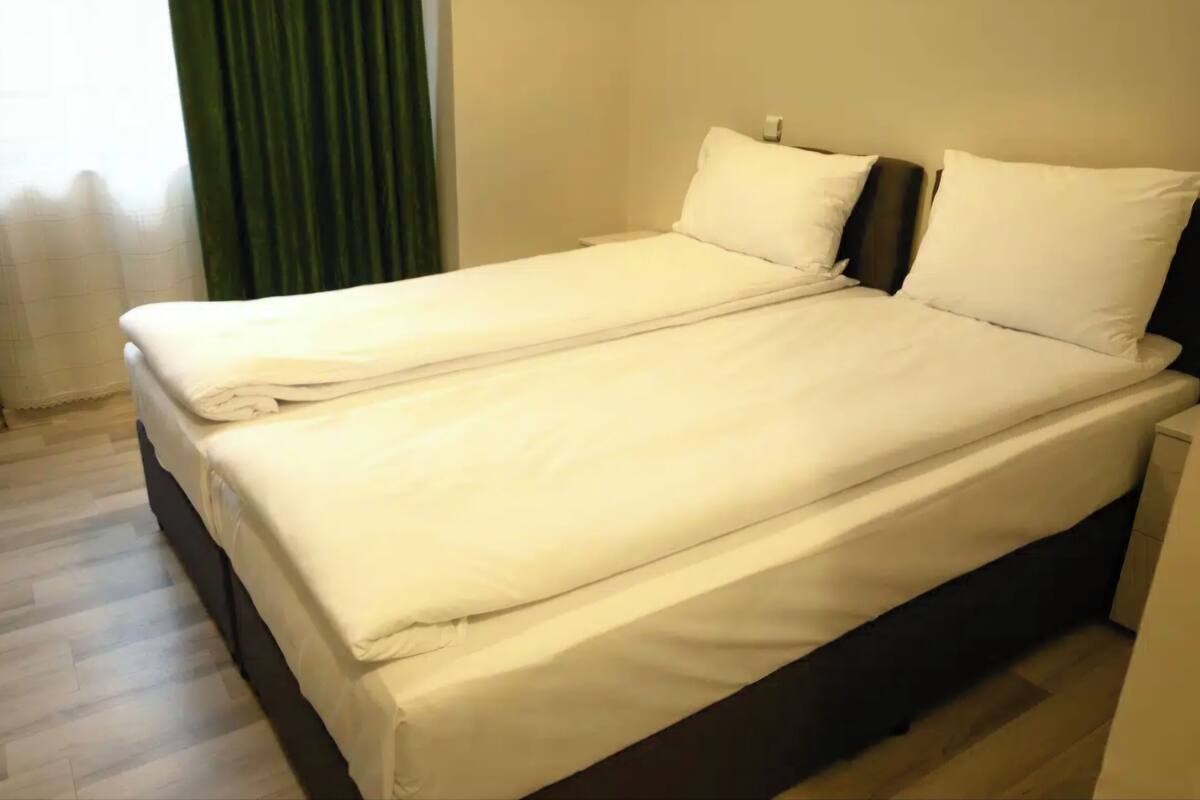 A double bed with white bedding, a dark headboard, and a wooden floor.