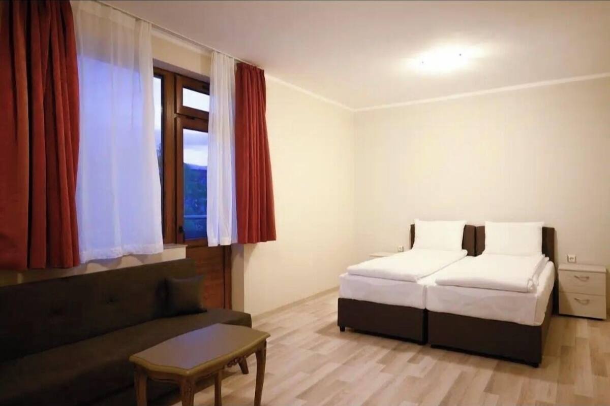 A room with a bed, a sofa, a small table, and a window with curtains.