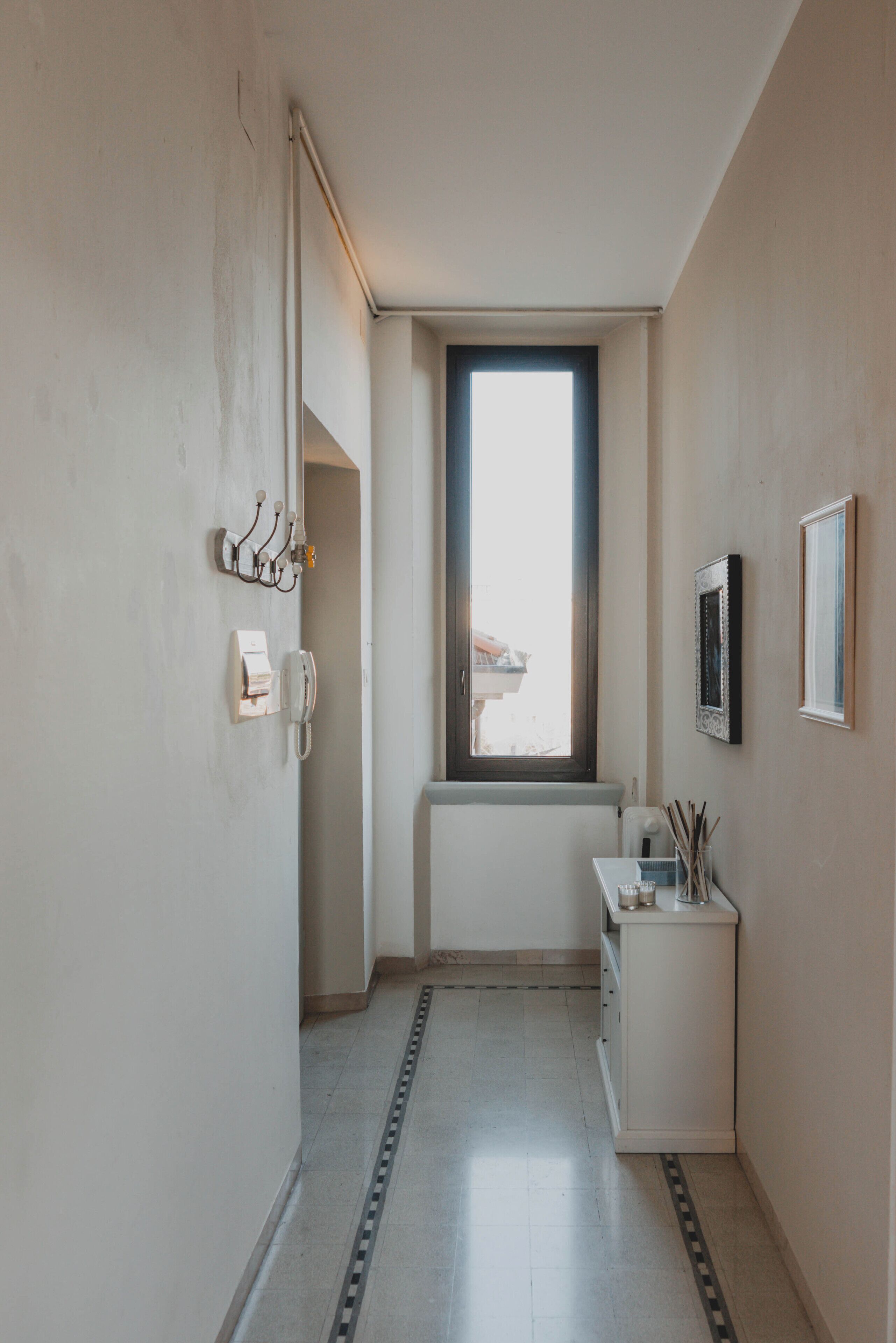A narrow hallway with a window, a small white cabinet, and a telephone on the wall.