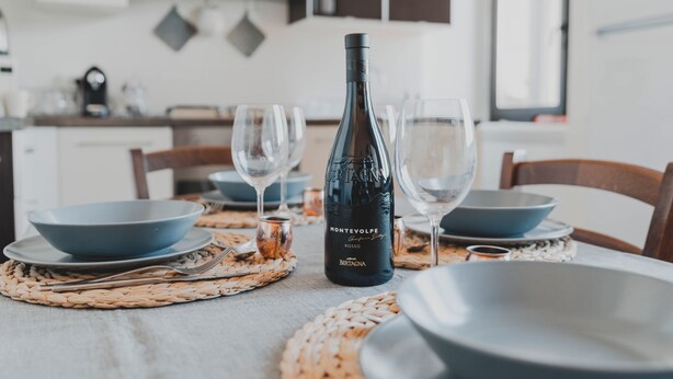 Mesa de comedor dispuesta con platos azules, copas de vino y una botella de vino Montevolpe.