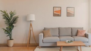 Una sala de estar con un sofá gris, una mesa de centro de madera, una lámpara de pie y una planta en maceta.